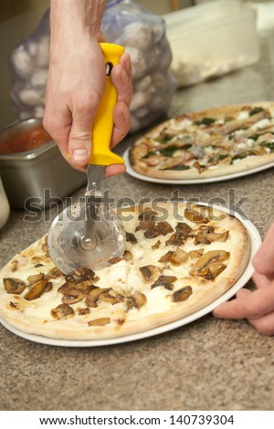 hand with a knife cut the pizza