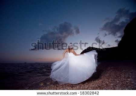 Bride posing showing her wedding dress on sunset beach