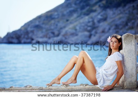 Portrait of beautiful brunette woman with long legs posing over sea view