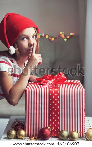 Portrait of a pin up kid girl holding big Christmas gift box on blue vintage wooden background