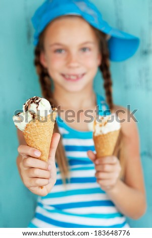 Portrait of 7 years old kid girl eating tasty ice cream on blue background