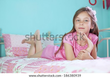 Portrait of 7 years old school girl resting on pink bed in her nursery at home