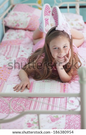 Portrait of 7 years old school girl reading a book on pink bed in her nursery at home