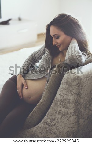Home cozy portrait of pregnant woman wearing warm cashmere sweater resting on a sofa at home