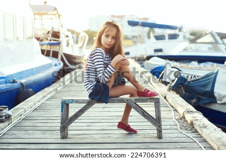 Fashion child wearing navy clothes in marine style posing on wooden berth in sea port