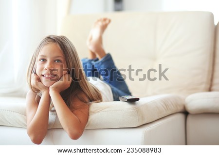 8 years old child watching tv laying down on a sofa at home alone