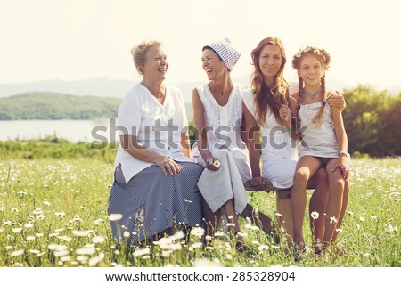 Four generations of beautiful women sitting together in a camomile field and smiling