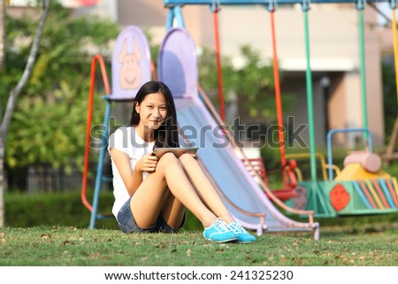 Tablet computer. Relaxed young teenage in garden smiling content, happy and reading on tablet pc at home in garden. Lifestyle image of beautiful mixed Asian Caucasian girl relaxing smiling happy