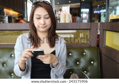 Cafe city lifestyle woman on phone drinking coffee texting text message on smartphone app sitting indoor in trendy urban cafe. Cool young modern mixed race Asian Caucasian female model in her 40s.