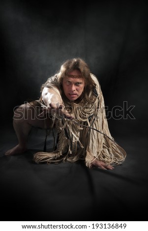 man with long hair in the ancient character stretches his hand to the camera on a black background