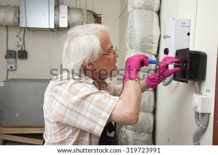 Man in pink gloves is fixing a broken ventilation stack with blue screwdriver in his hands