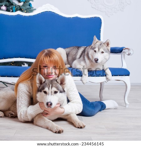 Young beautiful woman with husky dogs on a blue sofa in a Christmas setting.