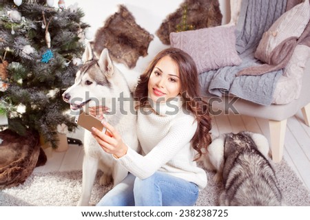 Young beautiful smiling brunette woman with phone in hand and dogs in a Christmas setting.Husky.