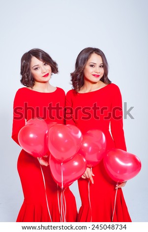 Two beautiful young woman in a long red dress with balloons in the form of heart in his hands. Valentine\'s Day. Twins.