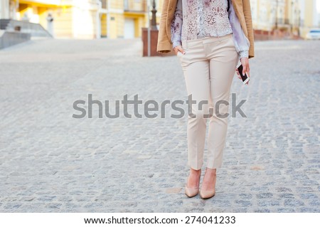 Detail of a beautiful young woman in trousers and high-heeled shoes posing in the city streets
