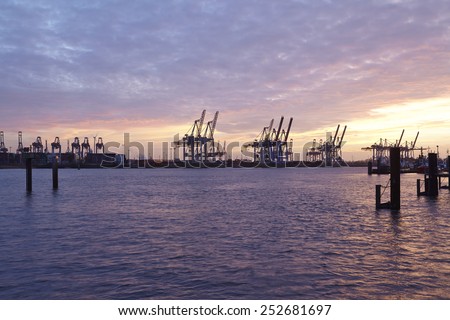 The Port of Hamburg with some container gantry cranes as silhouettes against the sky taken in the evening at the point of the blue hour.