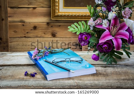 Flower and Yellow Glasses place on note books with flowers vase on wooden table.