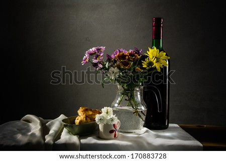 still life bread and wine and a vase of flowers on the background of old pictures.