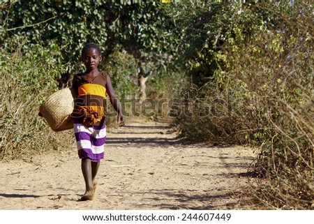 Poor african girl walking the sandy path with basket in hand