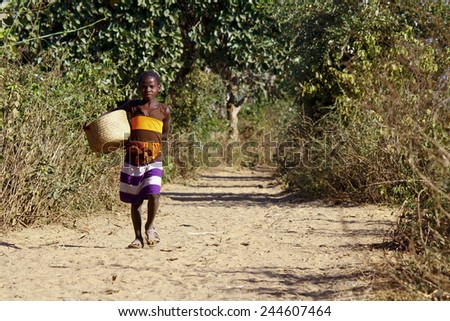 Poor african girl walking the sandy path with basket in hand