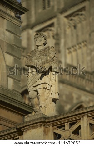 Old weathered stone statue above the ancient Roman Baths in Bath, Somerset, England. Bath Abbey in the background.