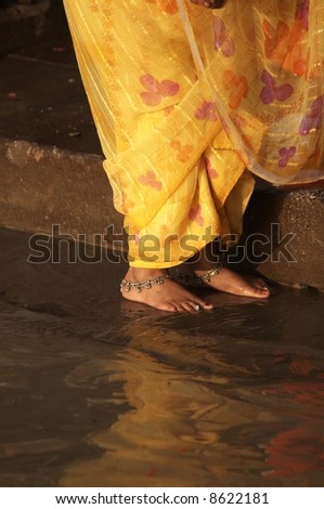 Woman in yellow sari standing on steps by rivers edge. Varanasi Uttar Pradesh India