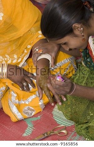 Indian lady applying ornate henna hand painting to the hand of another Indian lady