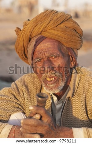 Old Indian man in a turban smoking a pipe at the Nagaur Cattle Fair in Rajasthan, India