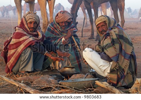Indian men wrapped in blankets clustered around an open fire at the Nagaur Cattle Fair, Rajasthan