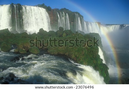 Large waterfalls with white water falling over cliff. Green vegitation and rainbow. Iguacu Falls, Brazil.