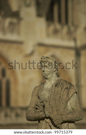Old weathered stone statue above the ancient Roman Baths in Bath, Somerset, England. Bath Abbey in the background.