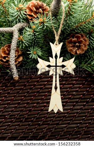 Wooden Cross Ornate laser cut wooden cross suspended by twine from a blue spruce branch. Above the cross are fresh cut blue spruce branches and pine cones.