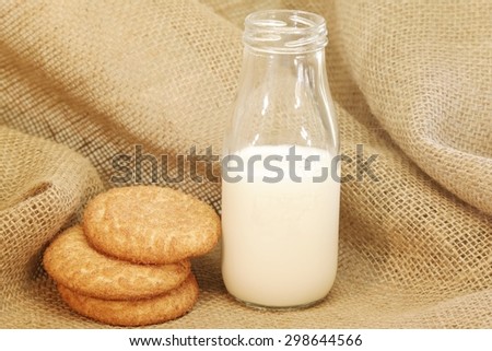 Milk and Cookies Three large snickerdoodle cookies beside a dairy bottle with milk inside. The cookies and milk have a burlap background.