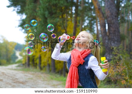 Five-year-old girl inflates soap bubbles outdoors