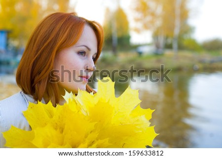 Portrait of the beautiful romantic woman with autumn leaves about a reservoir