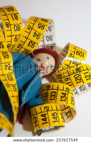 Red hair doll figure wearing blue dress resting nearby a measuring tape