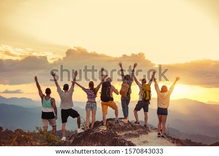 Group of happy friends stands with raised arms at sunset mountain and enjoys sunset ストックフォト © 