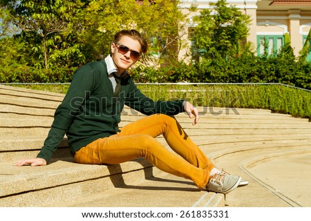 Fashion man in sunglasses, jacket and jeans is sitting on stairs