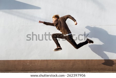 Man with funny long shadow jumps on background of white wall