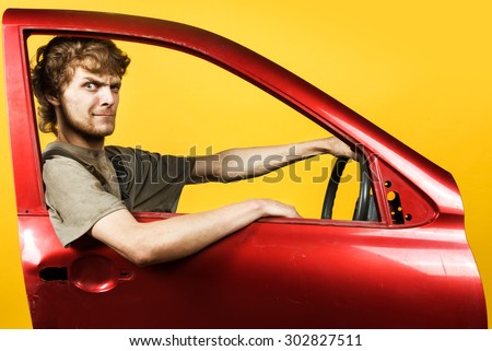 Mad worker, dressed in a dirty boilersuit, is leaning on a red car door, holding steering wheel in hands on yellow background