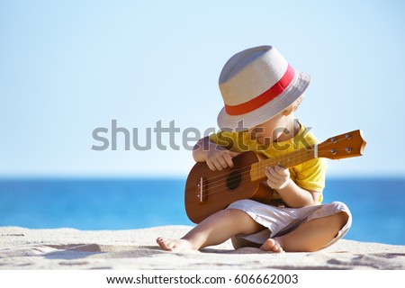 Little boy plays on Hawaiian guitar or ukulele at sea beach background. Space for text ストックフォト © 