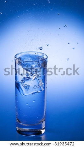Splash of mineral water and  falling ice cube into a transparent glass over blue gradient background