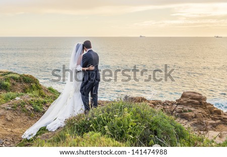 backs of bride and groom against landscape at dawn in italy