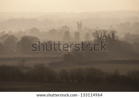 View of English countryside in the mist with a village and its church at the center of the scene