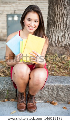 young female holding books looking at the camera whilst seated in the street