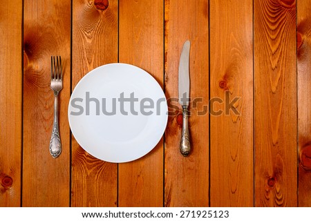 Empty white round plate with antique knife and fork on wooden background. Top View with text space.