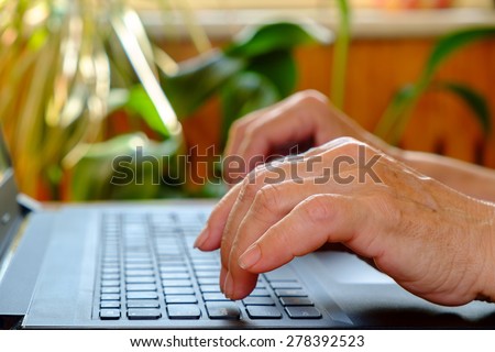 Elderly women\'s hands is typing text on the laptop. Closeup, side view
