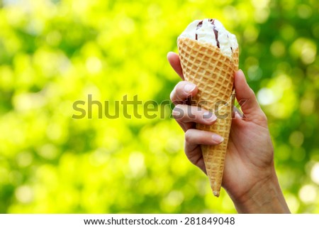 Cone ice cream in women\'s hand on natural green background