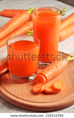 Glass of carrot juice and fresh carrots on white wooden background