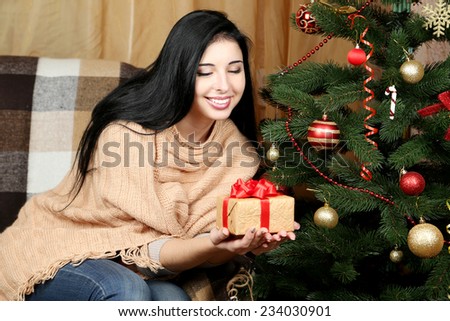 Young beautiful woman with gift box on sofa near christmas tree